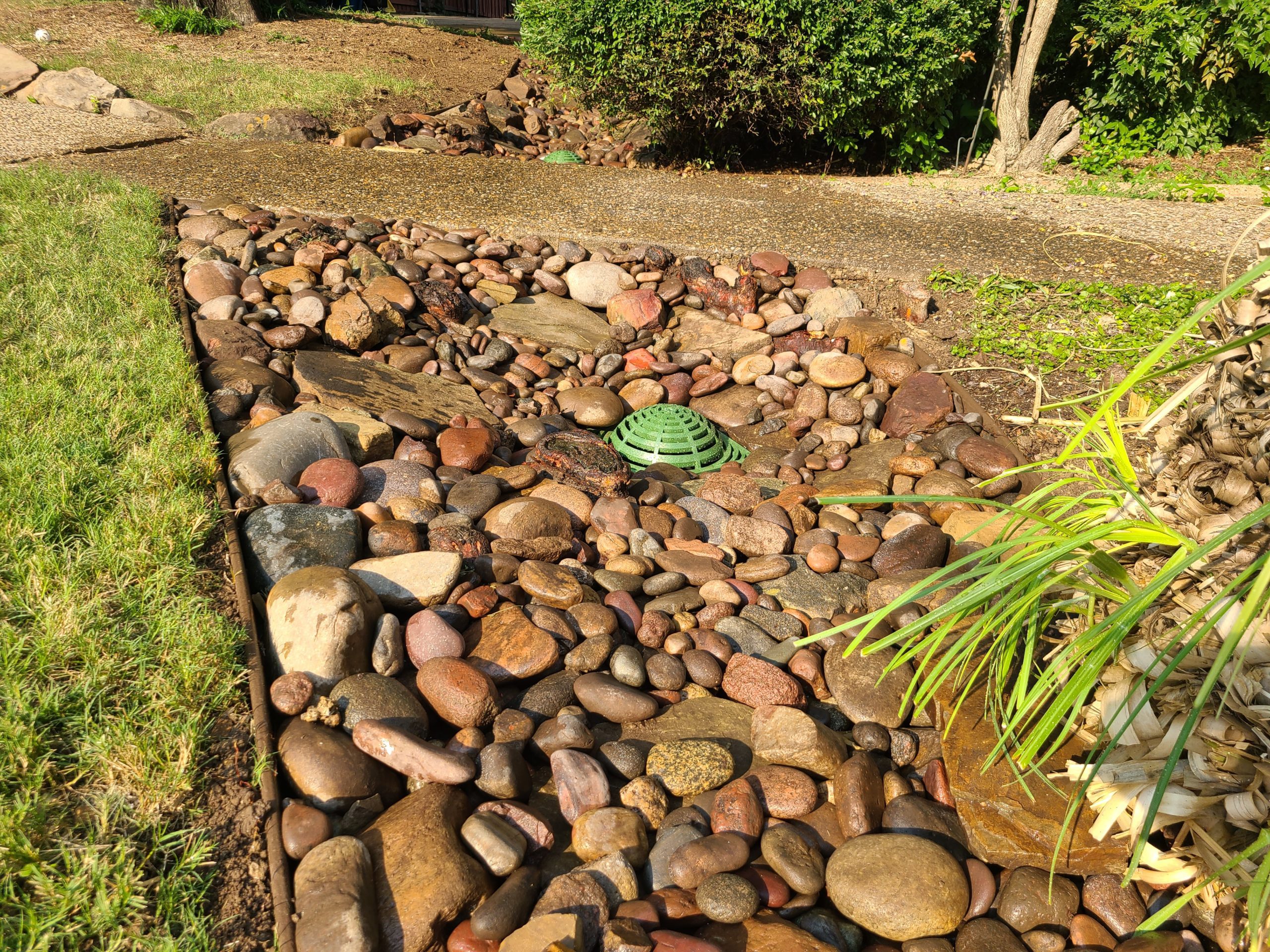 A lawn with some small rocks and a drainage system at the middle